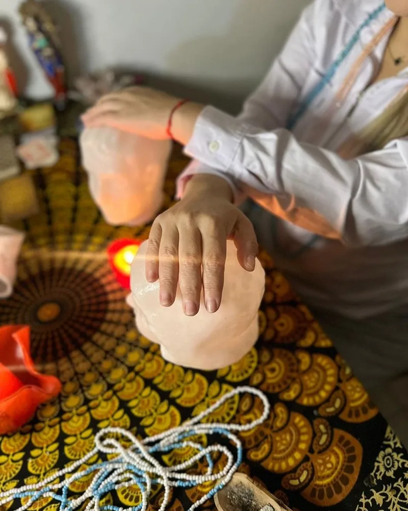 Mãos conduzindo um trabalho de limpeza espiritual com velas e cabeças de cristal