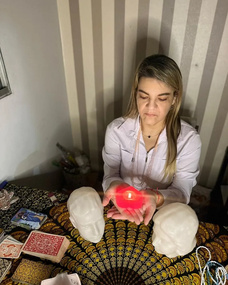 Cigana Laura à mesa de trabalho, com cartas, cabeças de cristal e vela acesa