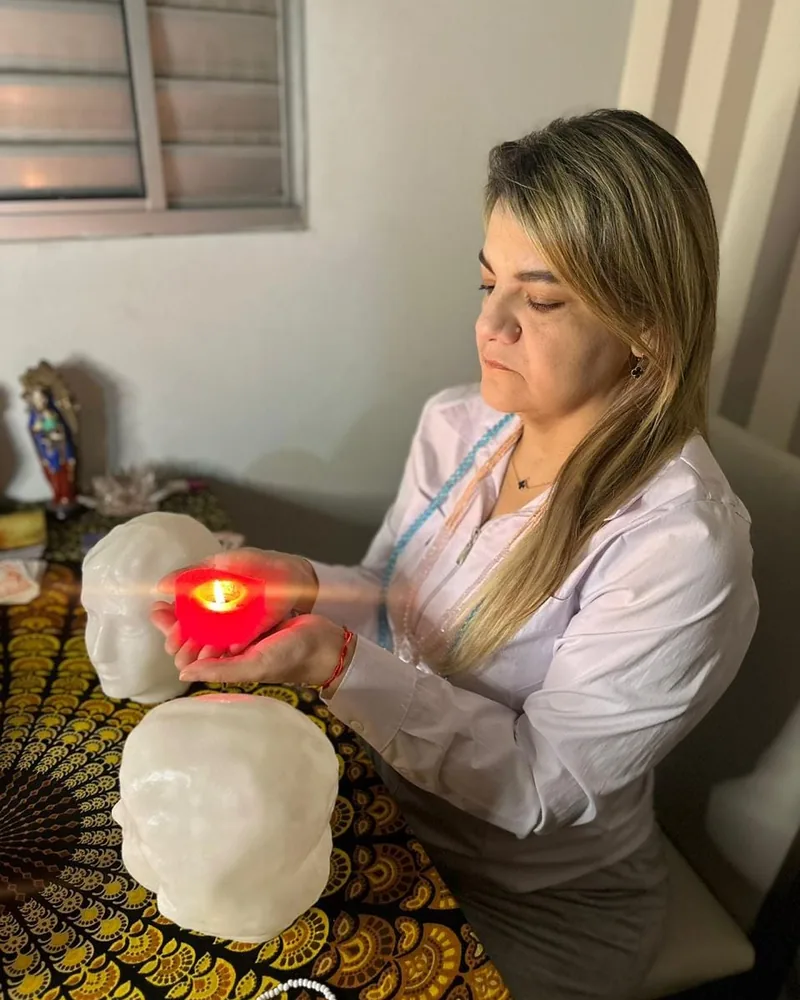 Cigana Laura segurando uma vela acesa entre duas cabeças de cristal