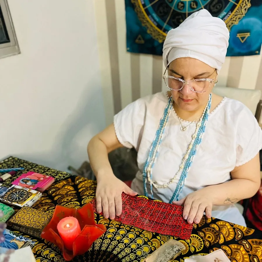 Cigana Laura em sua mesa de atendimento, com o Baralho Cigano, vela e o painel de astrologia ao fundo